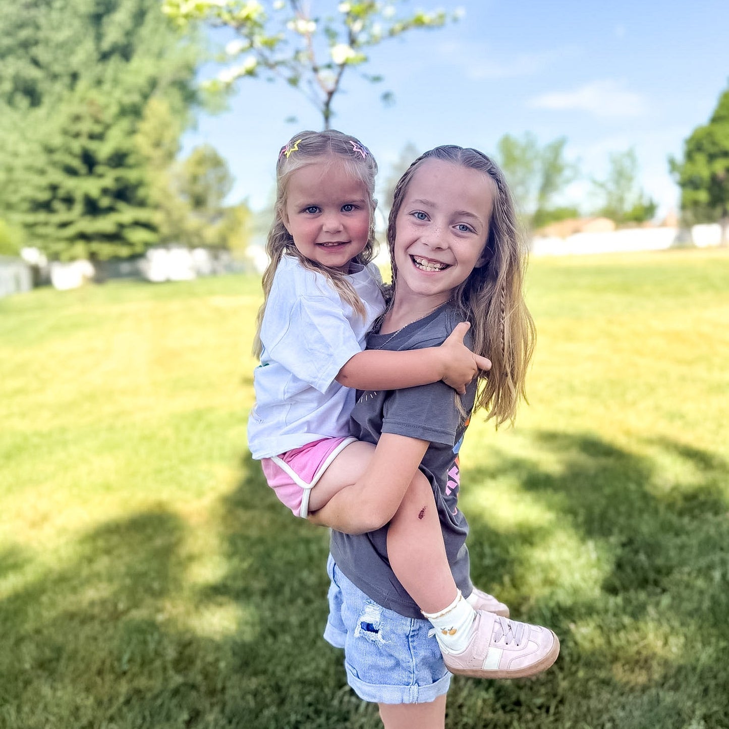 Two young girls playing in a grassy park on a sunny day.