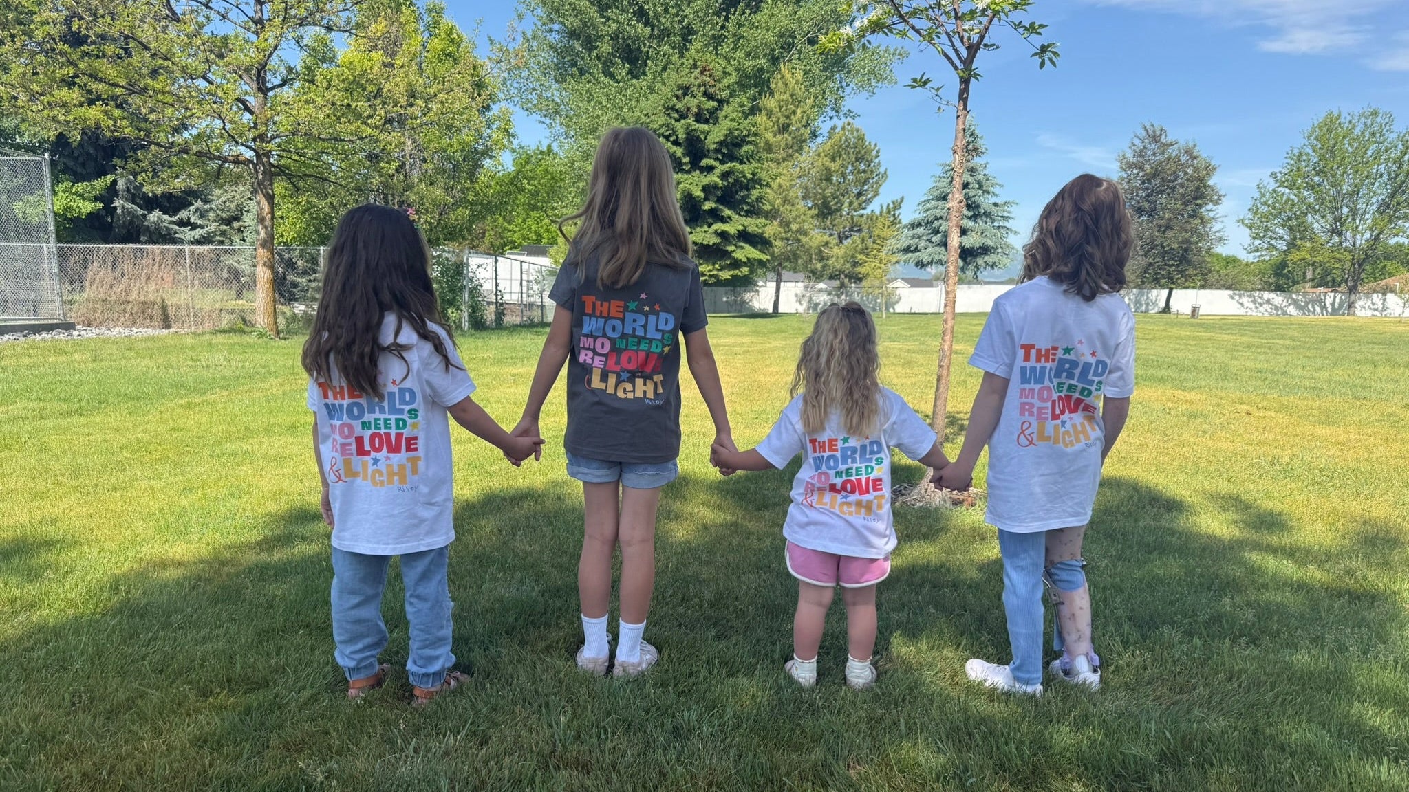 Four children holding hands in a park with t-shirts on displaying messages.