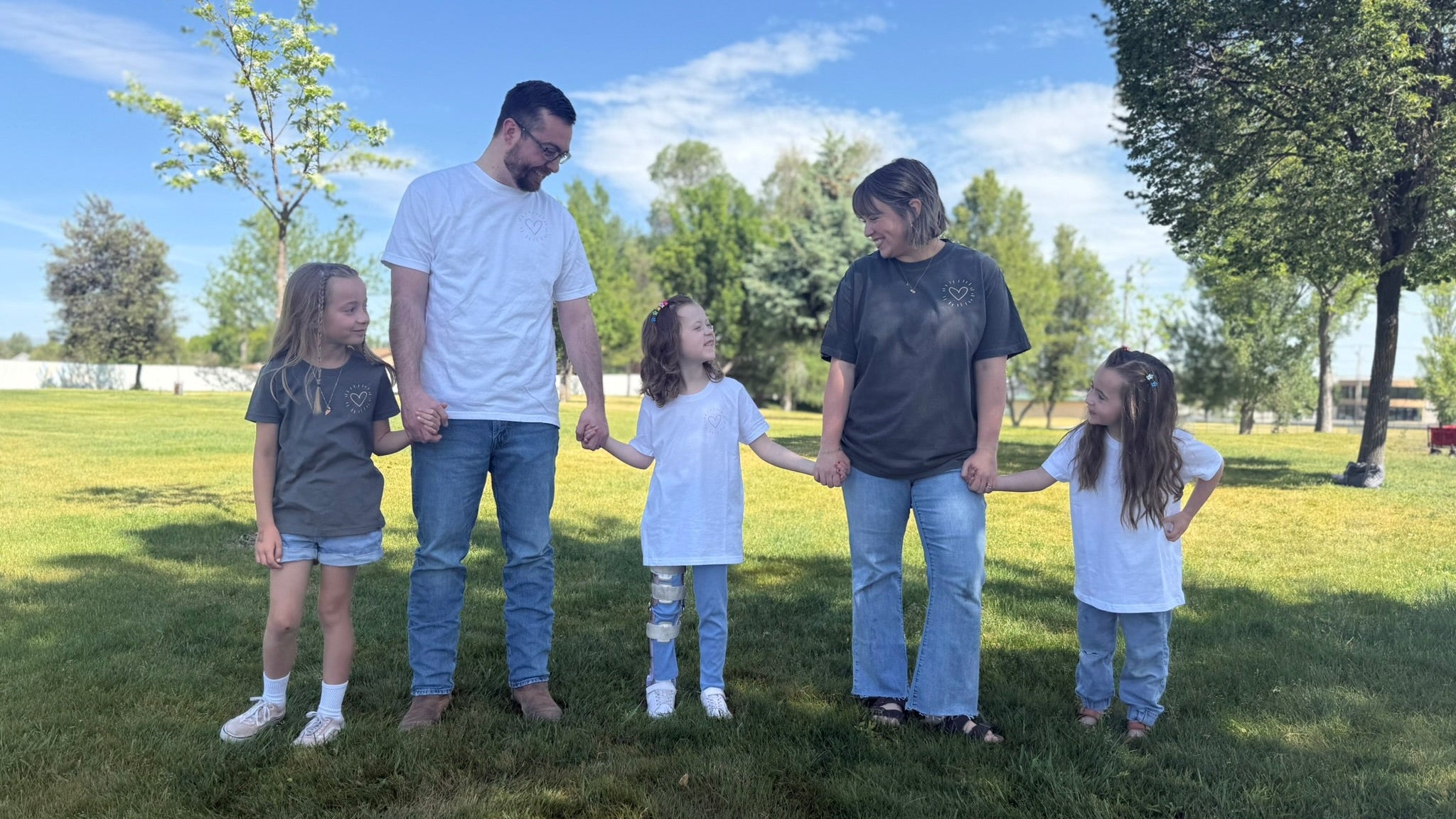A family of 5 holding hands in a park.